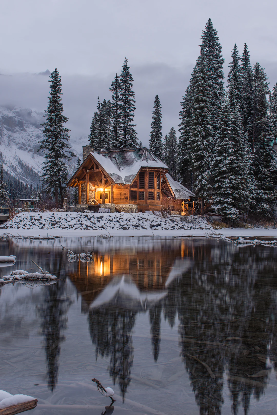 Chalet en bois éclairé au bord d’un lac, sous la neige