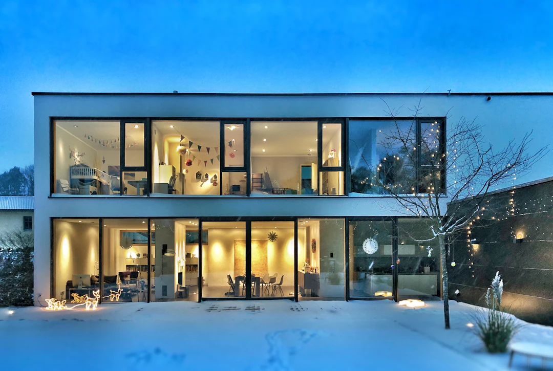 Maison contemporaine aux fenêtres illuminées à l’heure bleue, en hiver